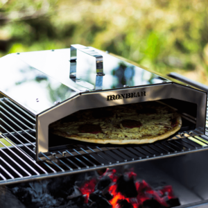 Durable Single Pizza Dome in use, placed on a stainless steel grill over a wood fire, ideal for outdoor pizza baking.